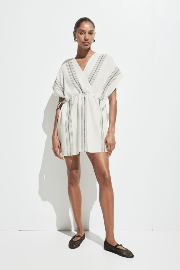 A short caftan-style dress in white with a waist tie and black stripe detail.