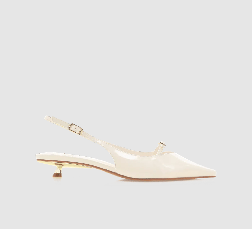 A pair of white patent leather kitten heels with a pointed toe and slingback.