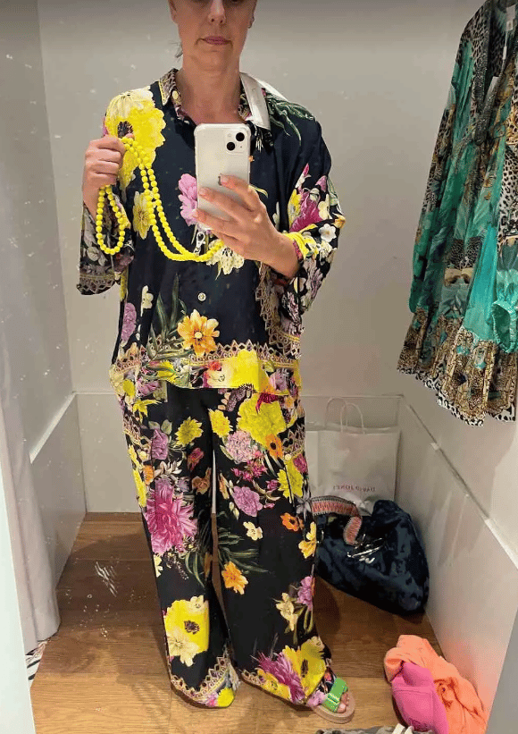 Mia Freedman takes a selife in a change room wearing a matching silk navy, purple and yellow floral set She's wearing bright green sandals and has a fluro yellow phone strap.