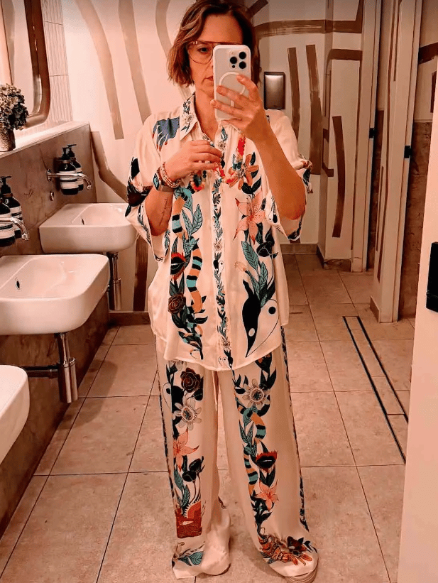 Mia Freedman takes a selife in a bathroom wearing a matching silk set It's white with a navy, pink and red floral design.She's also wearing a pair of glasses and has a stack of colourful bracelets and an Apple Watch on her wrist.