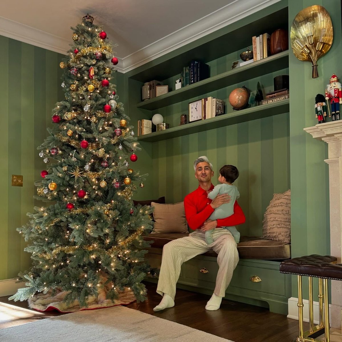 Tan France poses with his traditional Christmas tree, with a baby on his lap.