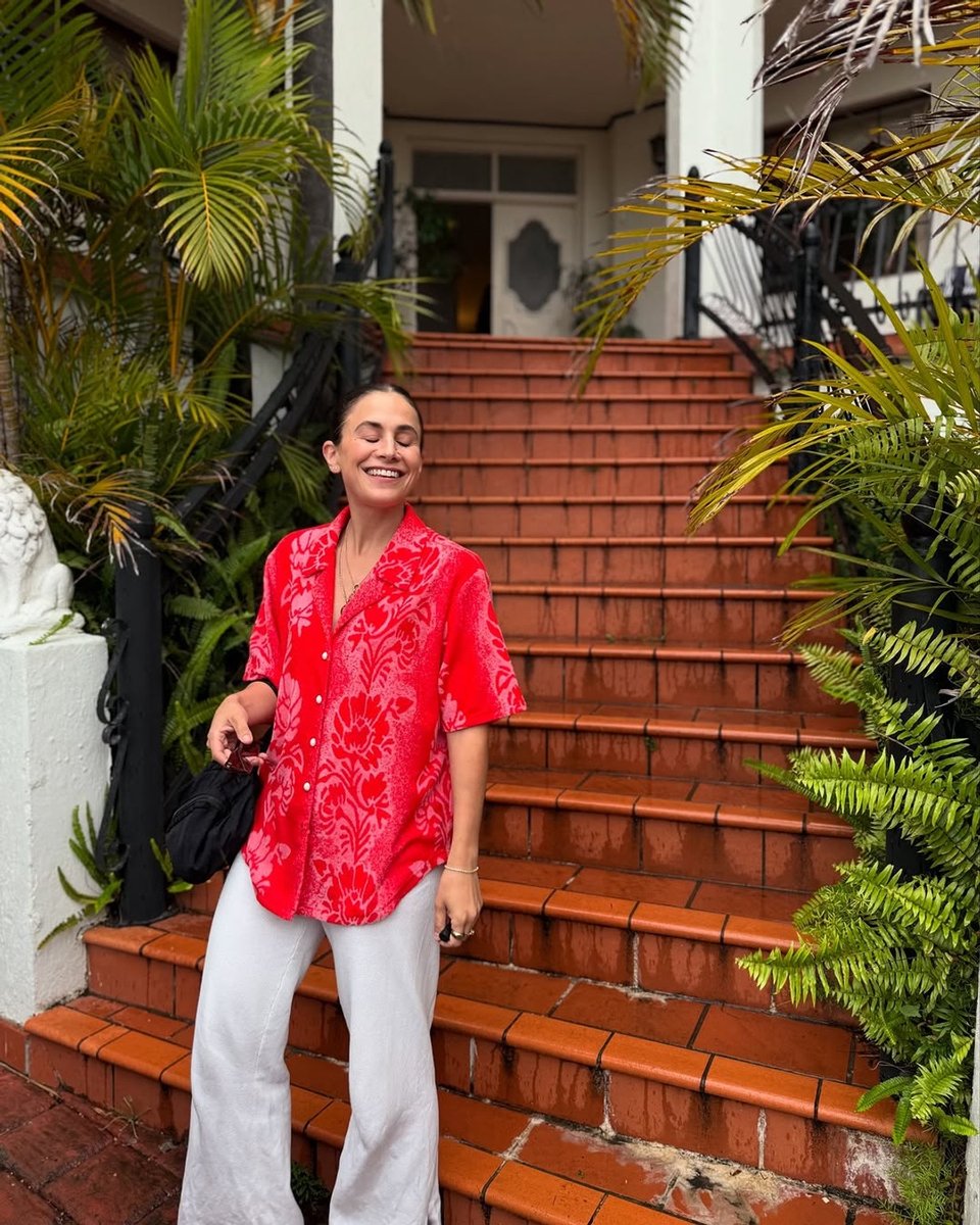 A woman wears a bright red velour floral shirt with white knit pants.