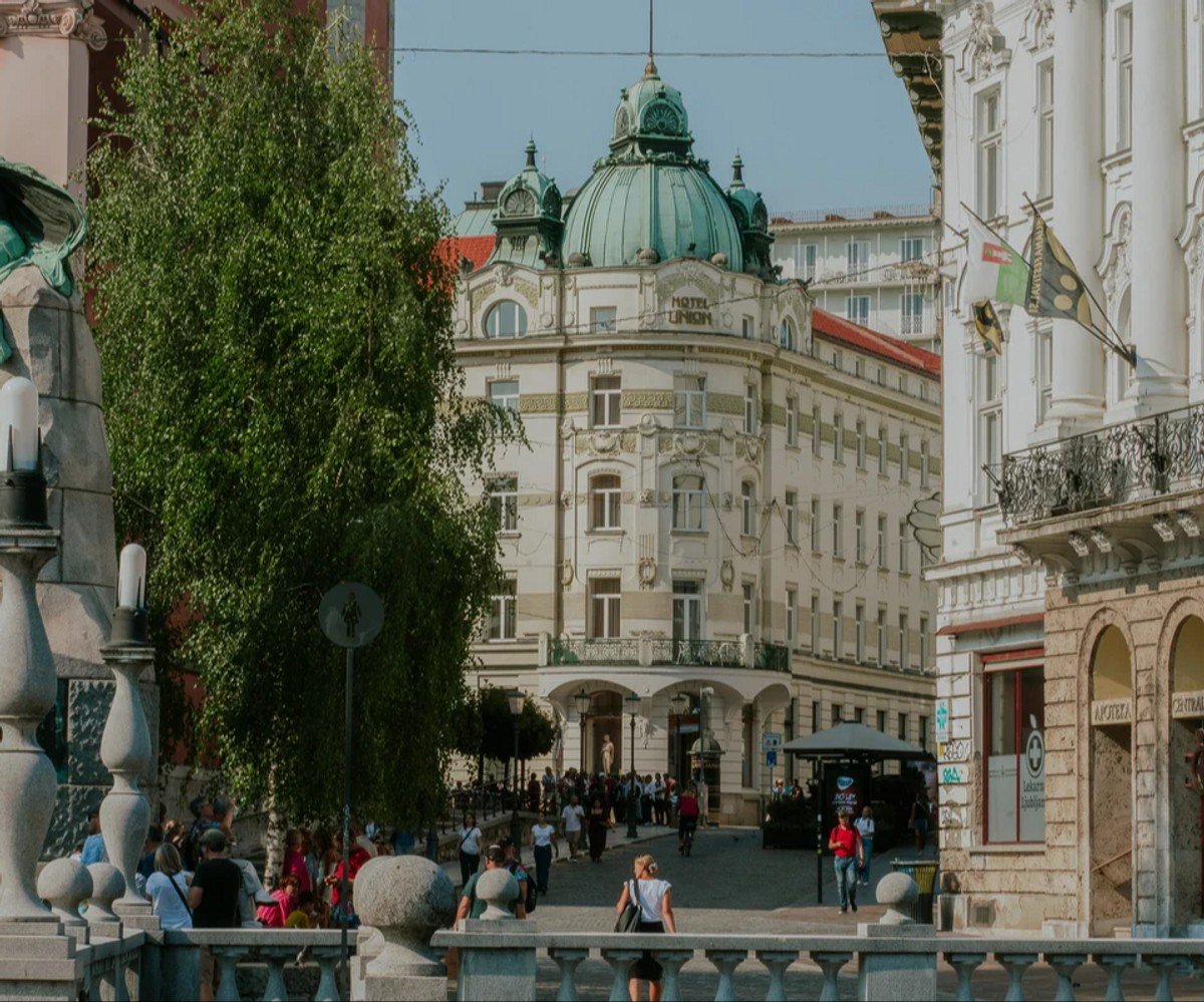 A lively picture of the Ljubljana streets, in the daytime, with the old architectural buildings in the background. 