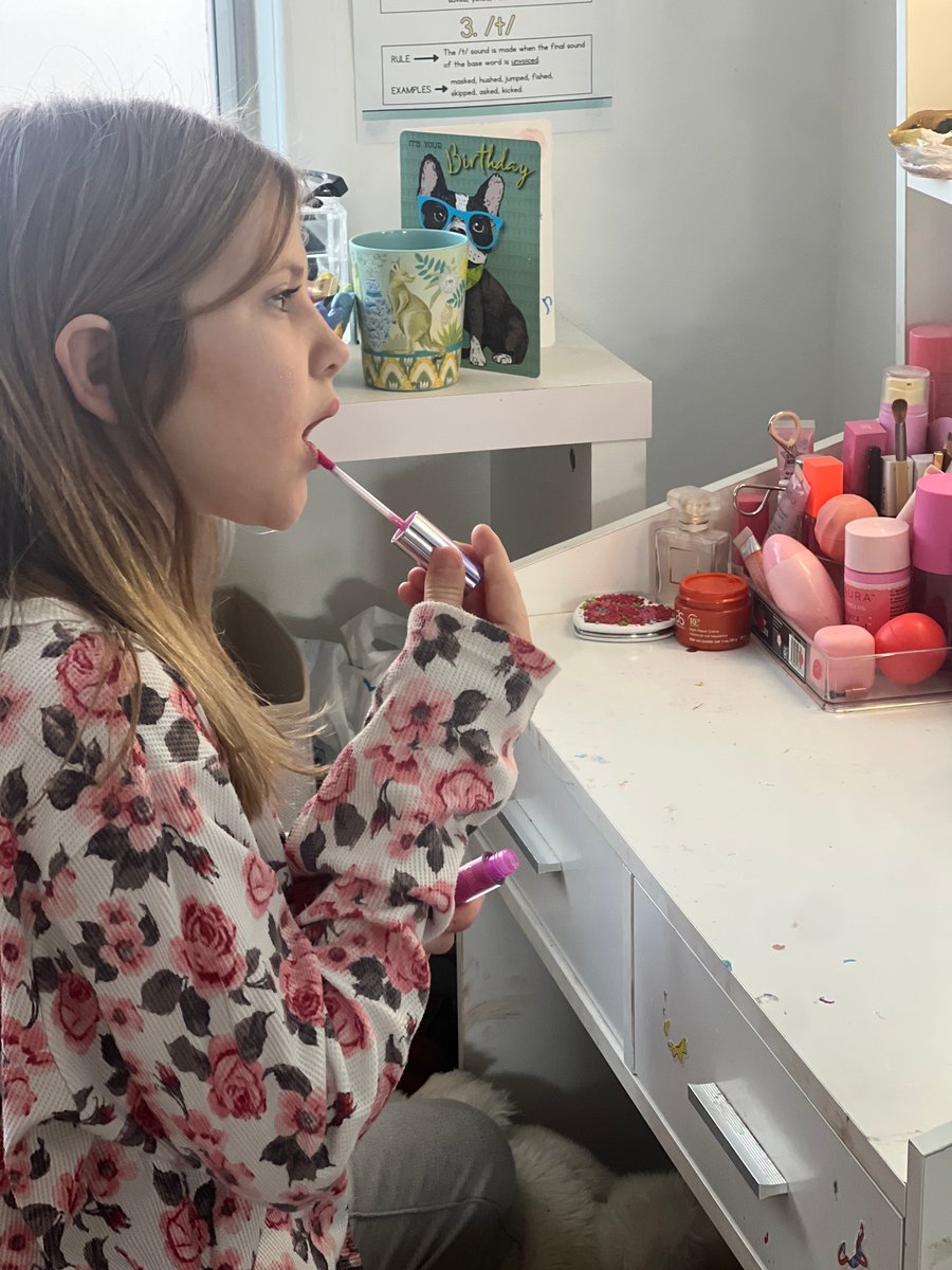 A young girl applies lip gloss while looking in the mirror.