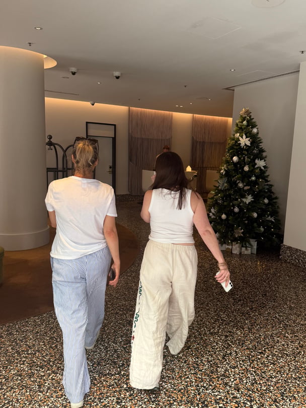 Two friends walk in hotel lobby with Christmas tree in the background.