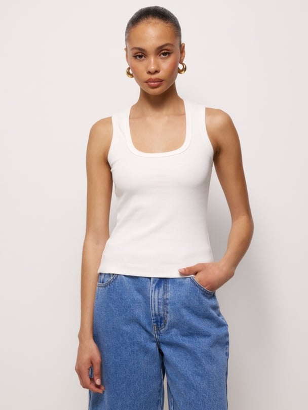 Model wears white scoop tank with blue jeans.