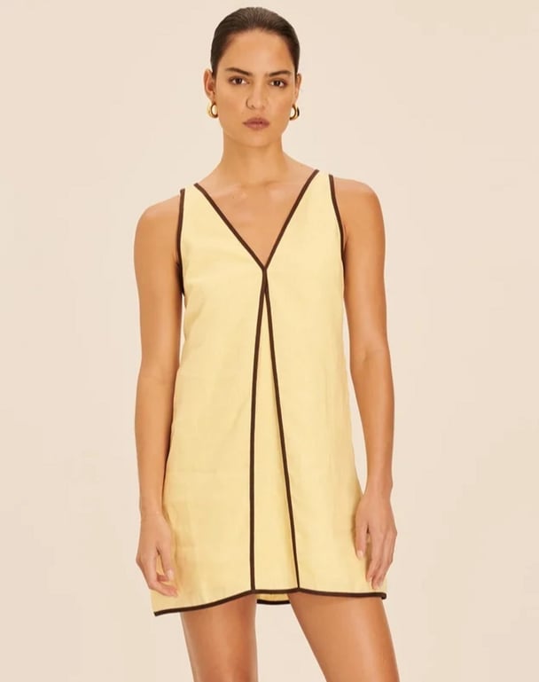 woman wearing pannelled butter yellow dress with brown trim