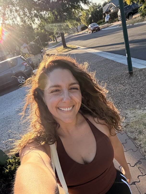 Alexia smiling while taking a walk outside, wearing a brown top.
