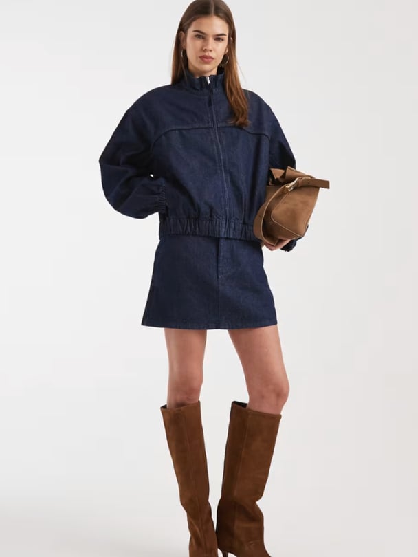 Woman wearing a zip-up denim jacket with a balloon-style sleeves and high-waisted denim mini skirt from asos.