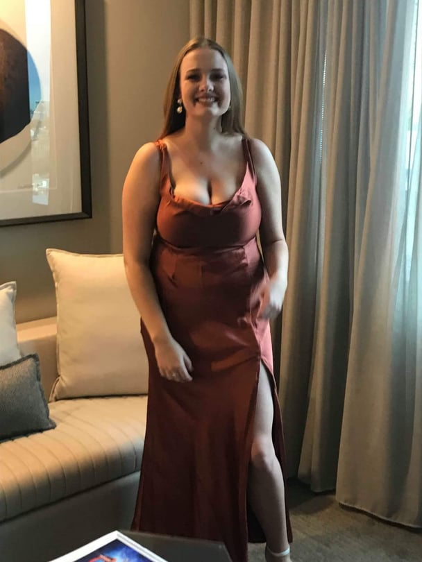 Natalie wearing a rust-colored dress with a high slit, standing indoors.