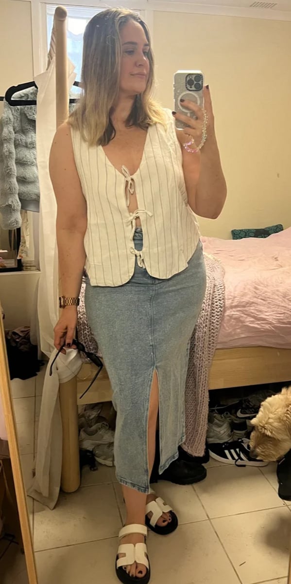 Woman wears white linen top and denim midi skirt, standing in a bedroom.