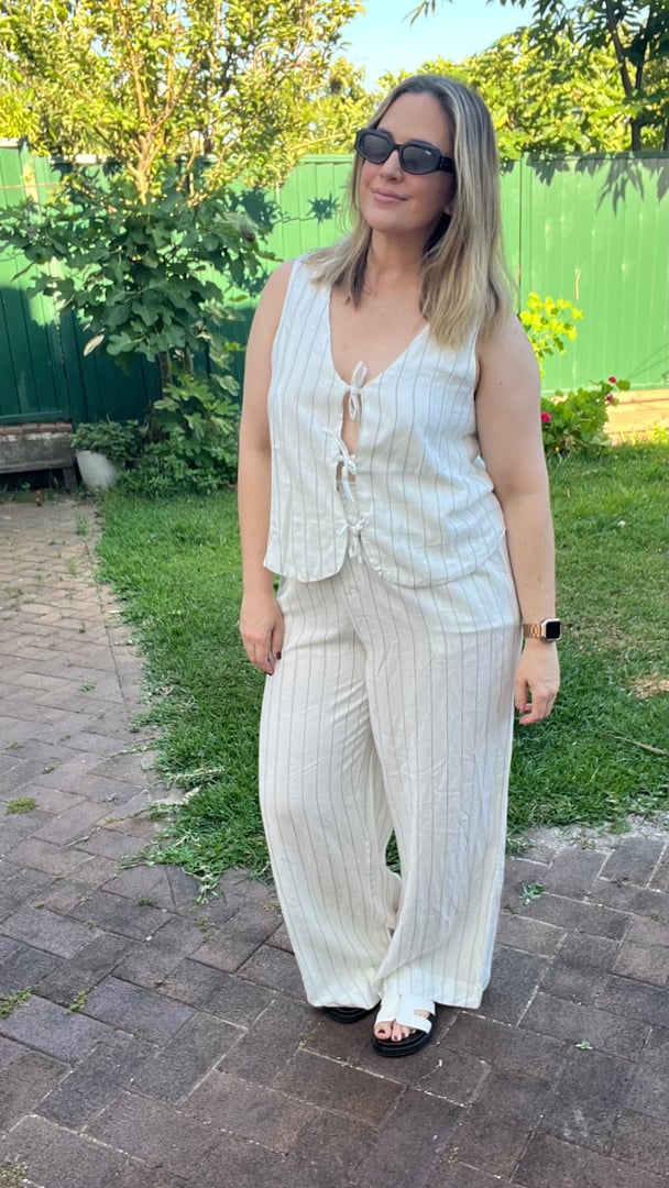 Woman wears white linen matching top and pants with pinstripes, standing in a garden.