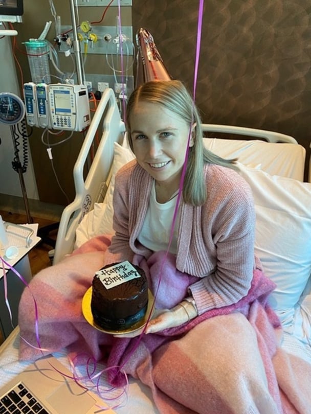 Olivia in a hospital bed wearing a party hat, holding a balloon.