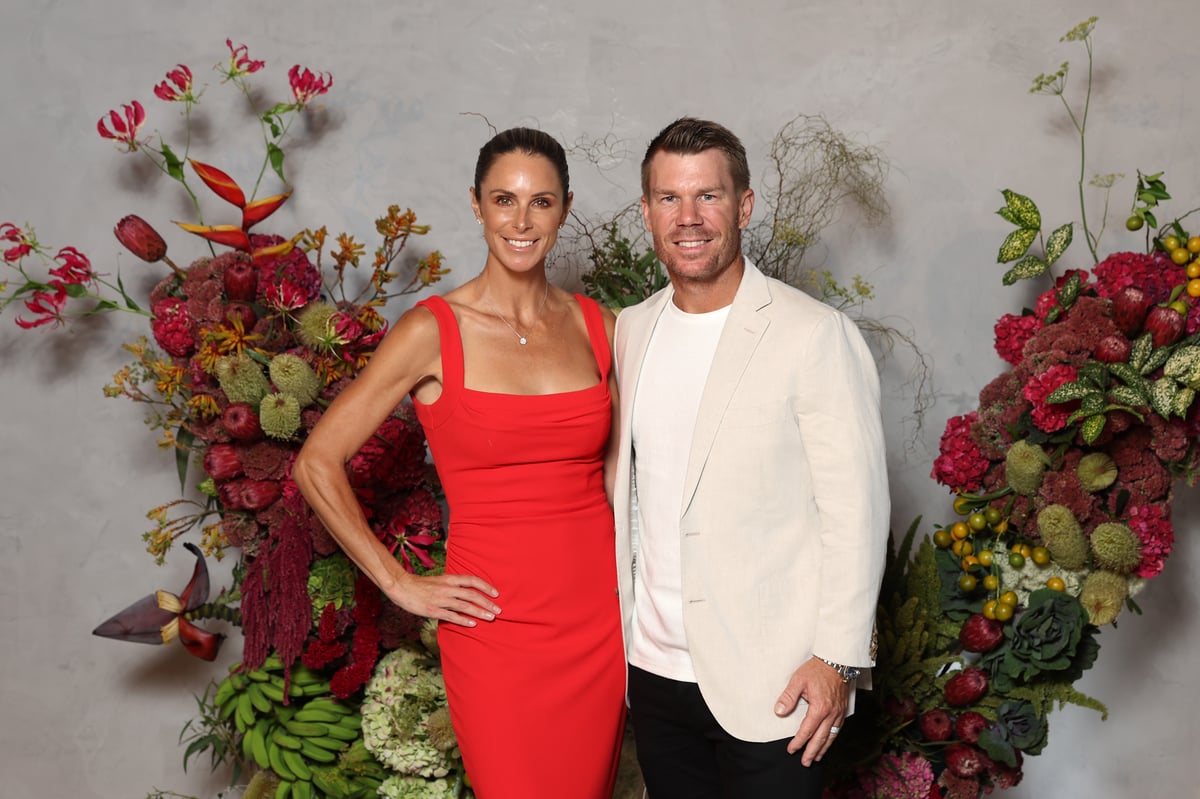 Candice and David Warner pose in front of a floral installation.