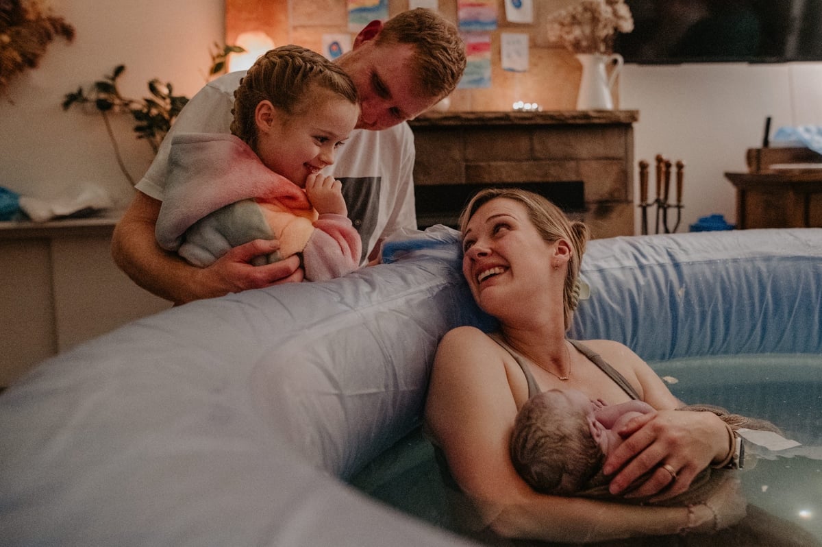 A father and young daughter smile at a mother who has just given birth at home.