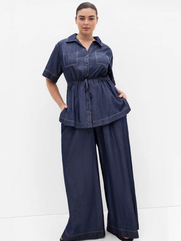Woman with dark hair pulled back in a bun wearing a dark-wash cotton denim shirt and pants from city chic.