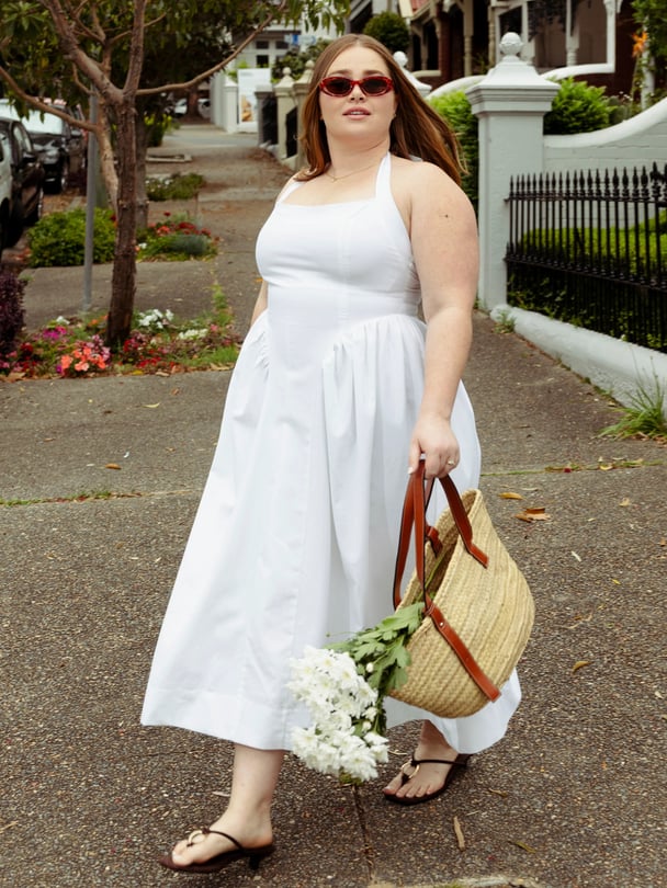 Model in white maxi dress holding basket bag with flowers.