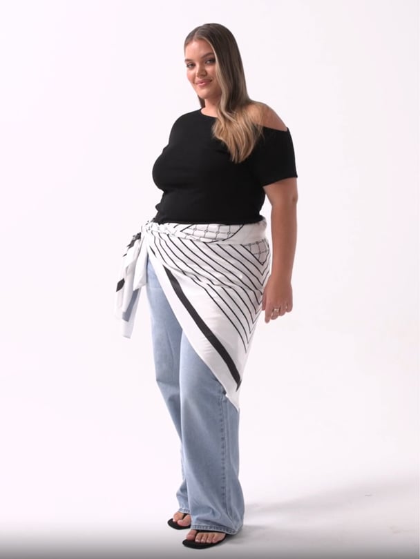 Model in black T-shirt and jeans with white and black scarf tied around waist.