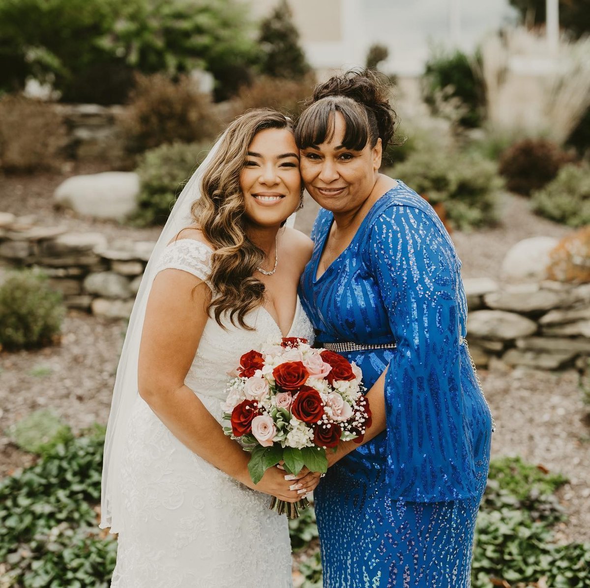 Delimar and mother Luz on her wedding day, Delimar wears an off-shoulder white dress and they have one hand each holding her bouquet.