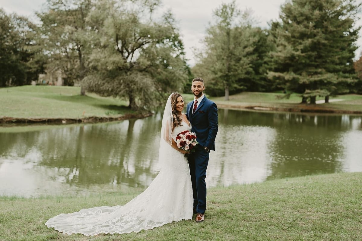 Delimar wears a white dress and poses alongside her husband Isaiah by a lake on their wedding day.