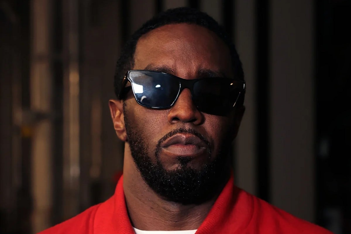 Sean 'Diddy' Combs with a surly expression wearing sunglasses and a red top.