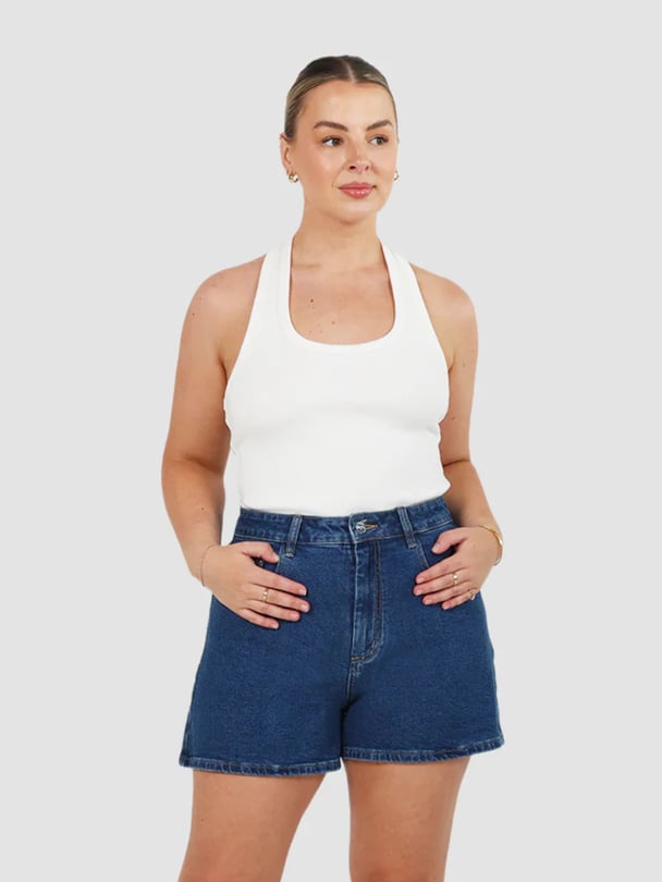 Model in white tank and dark wash denim shorts.