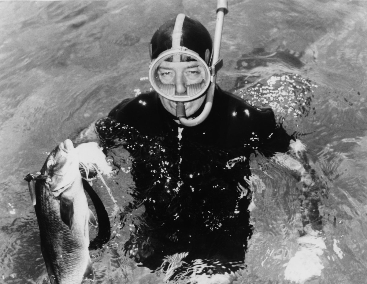 Harold Holt poses in the ocean with a snorkel and fish. 