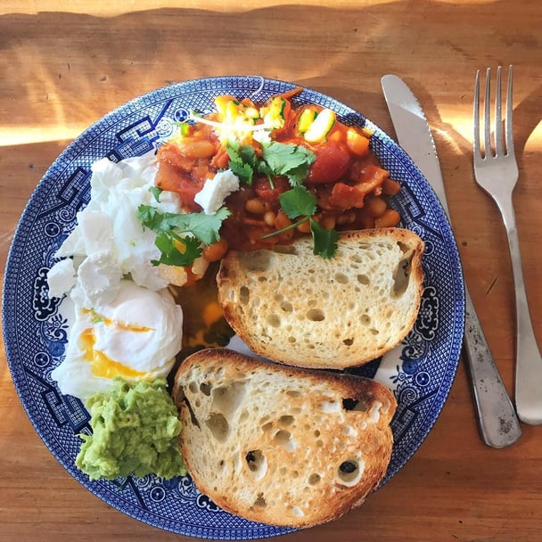 A plate of poached eggs, smashed avo and homemade healthy baked beans with toast.
