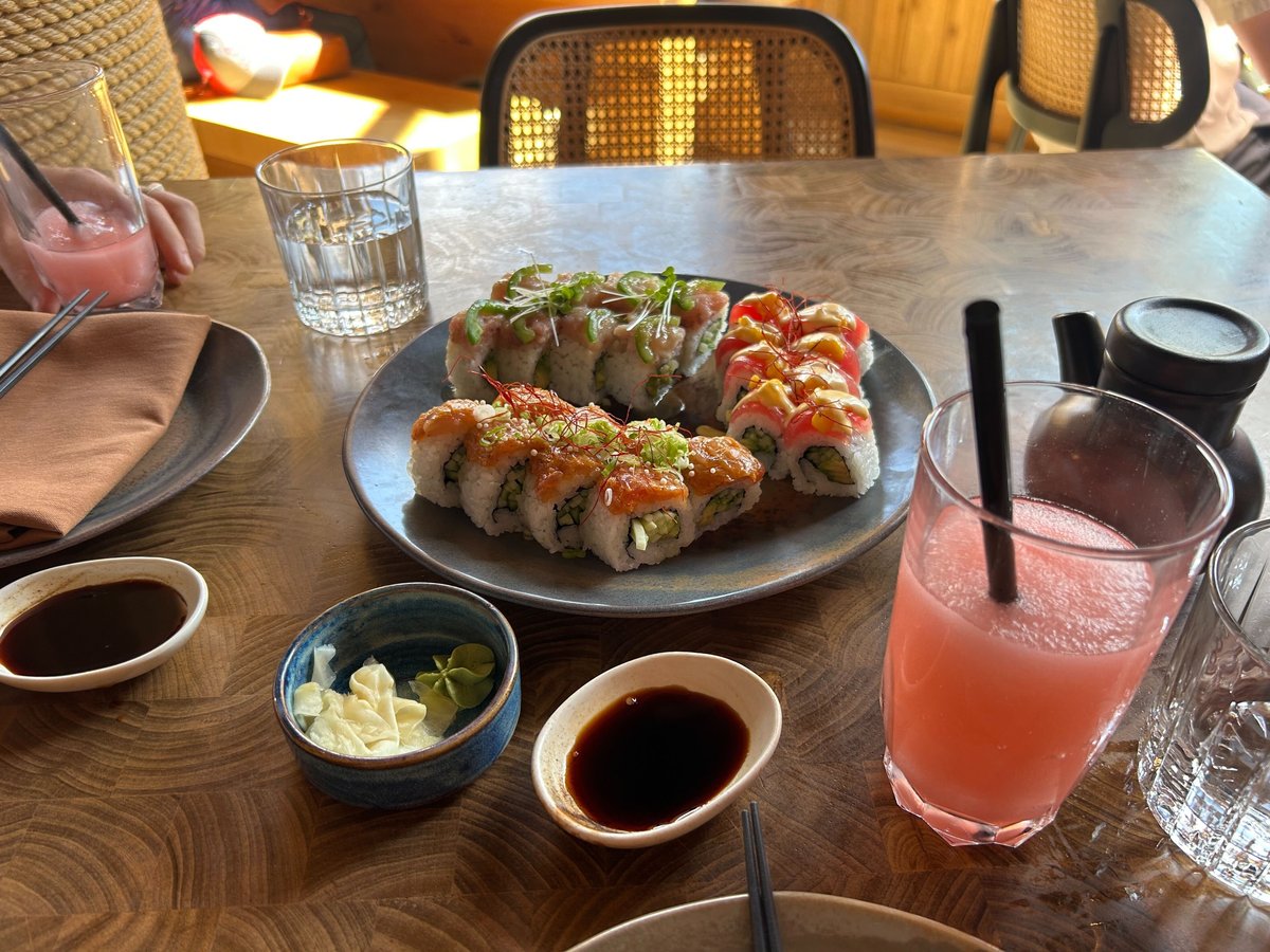Plate of sushi and a pink cocktail on dining table.