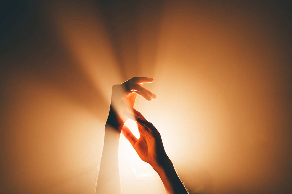 Non-sexual intimacy, such as holding hands can be a great way to get out of a sex rut. In this photo two hands touch with the sun behind them.