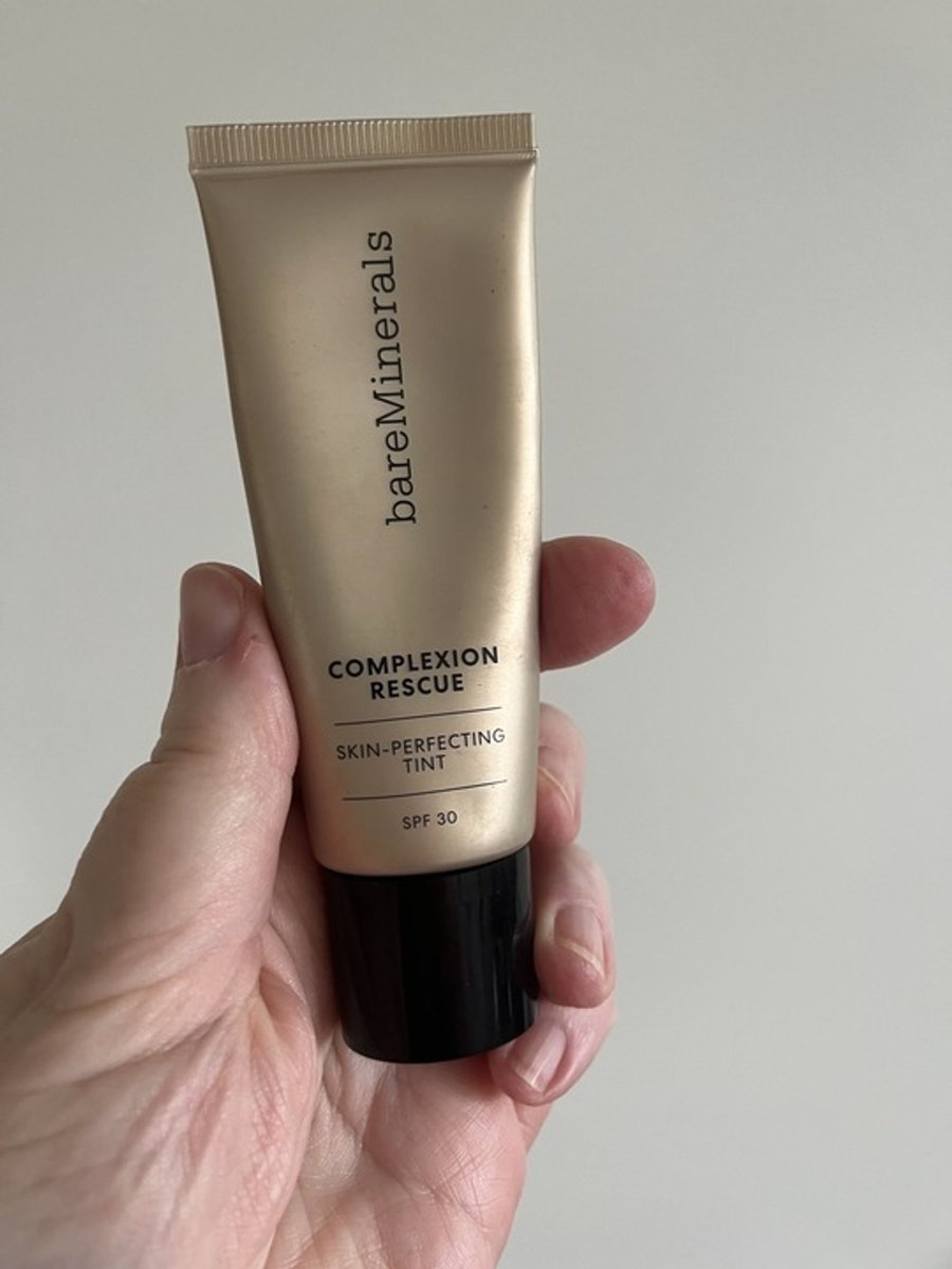 A hand holding up Bare Minerals Complexion Rescue.