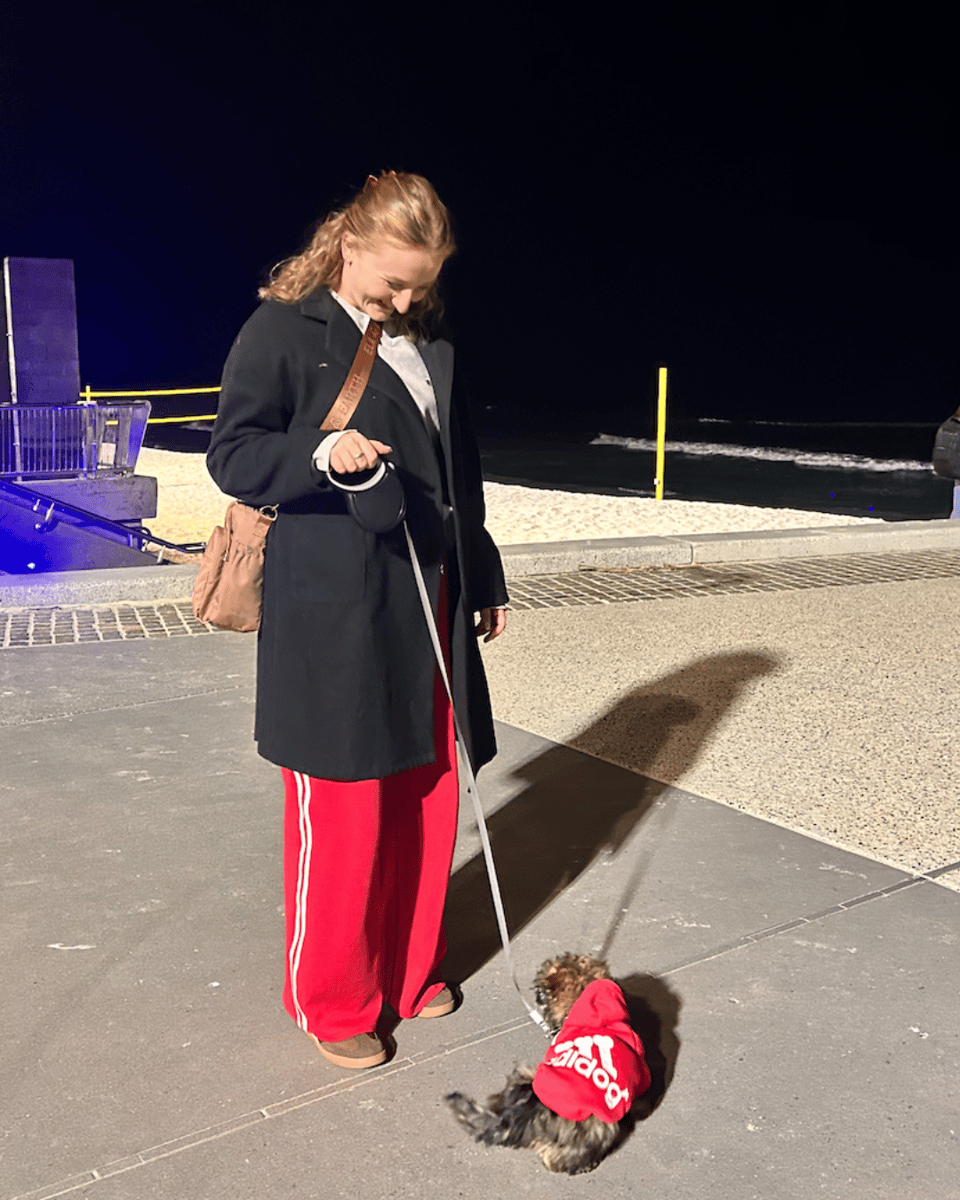 Jess walking her dog wearing a red 'Adidog' jumper. Jess is wearing matching red trackpants.