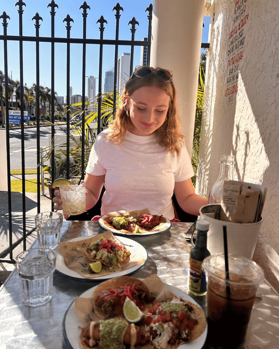 Jess Kenyi smiling with a margarita and tacos on an outdoor table.