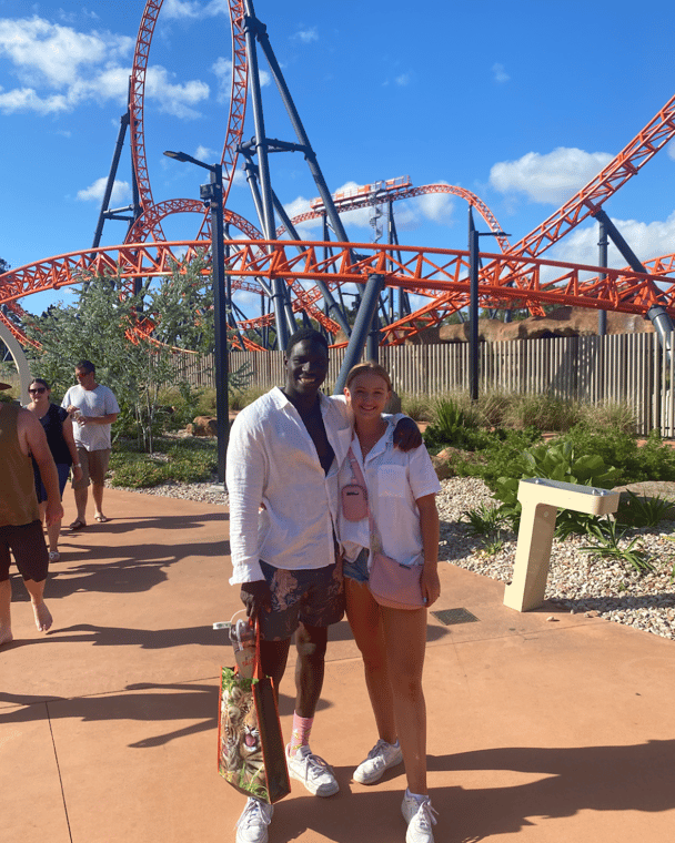 Jess and her partner smiling in front of large rollercoaster.