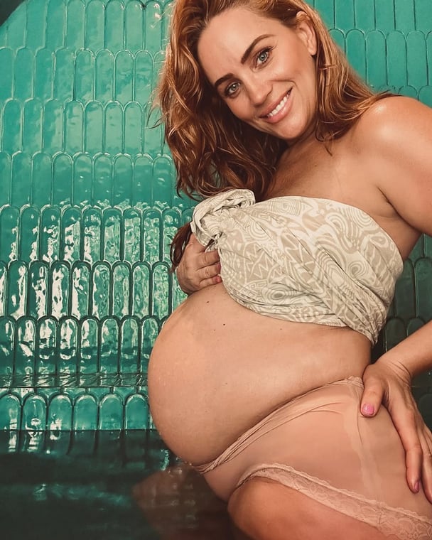Jules Robinson smiles while showing her pregnant stomach.