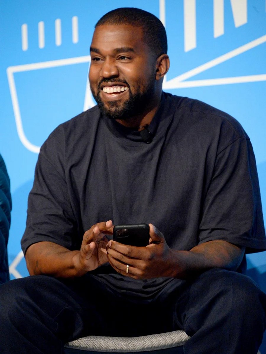 Kanye West smiling on stage as he speaks at the 