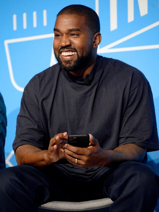 Kanye West smiling on stage as he speaks at the