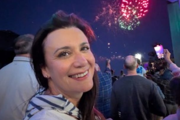 Kate smiling at the camera while fireworks explode in the background.