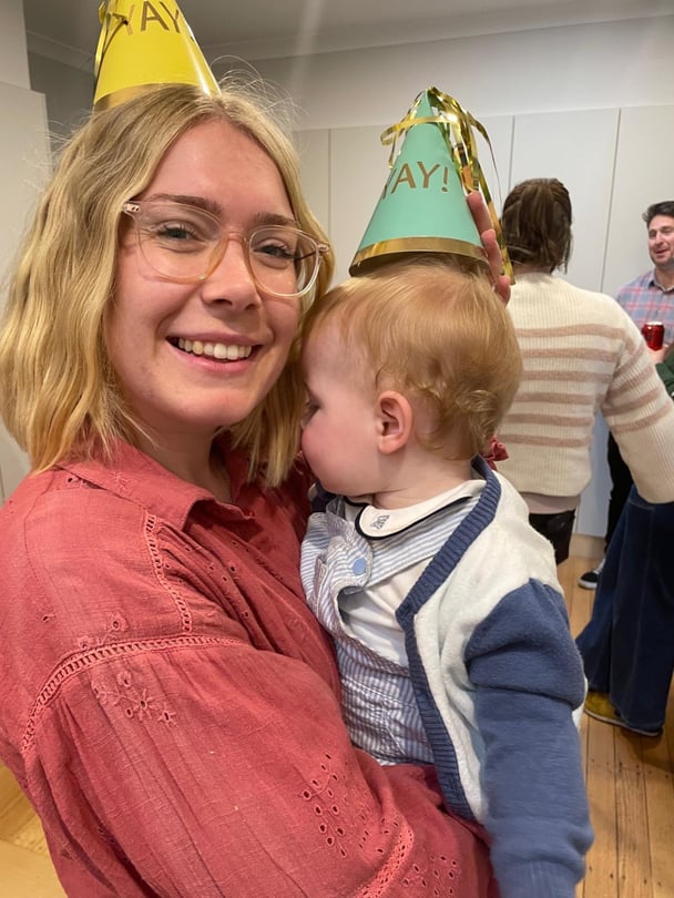 Katrina holding her baby at a birthday party wearing party hats.