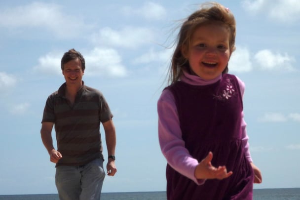 Kelsey as a child running on the beach with her dad running behind her.