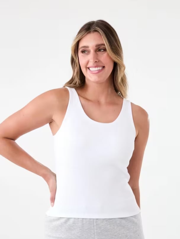 Model wears white tank with in-built bra and grey trackpants.