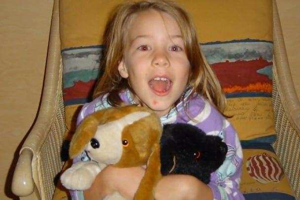 Darcie as a young girl holding two stuffed puppies.