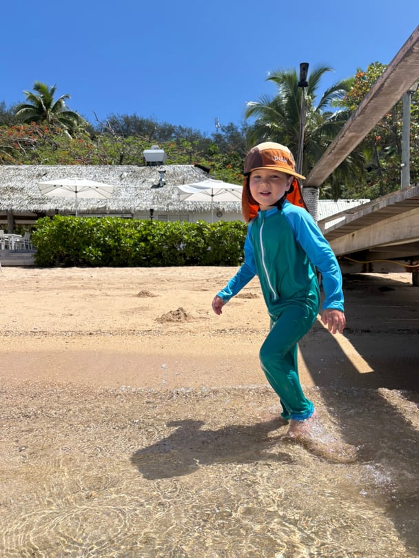 Zoe's son in the ocean in full body swimsuit and hat with neck protection.
