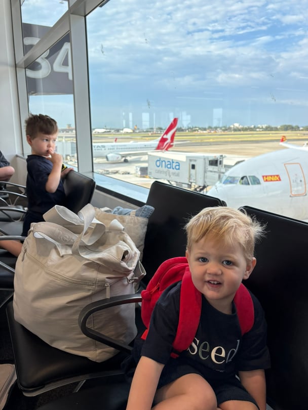 Zoe's toddlers sit next to large white nere travel bag.