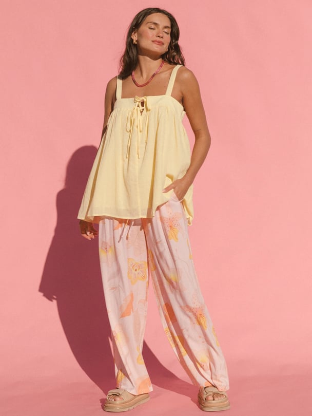 Model in front of pink backdrop in yellow singlet and pink floral pants.