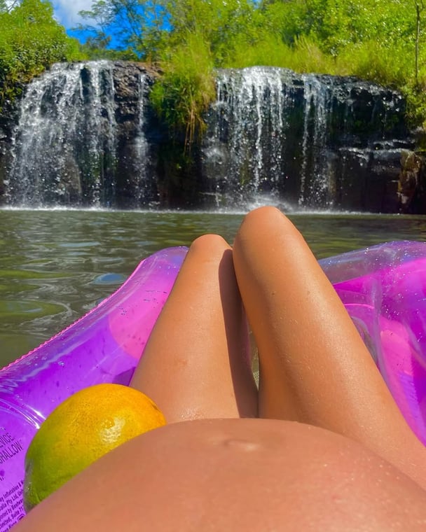 Madeleine West shows off her baby bump while laying on an inflatable in front of a waterfall.