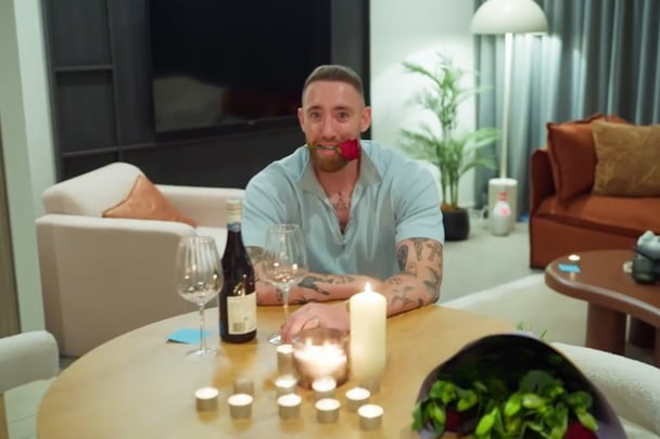 Danny with two glasses of wine with a rose in his mouth.