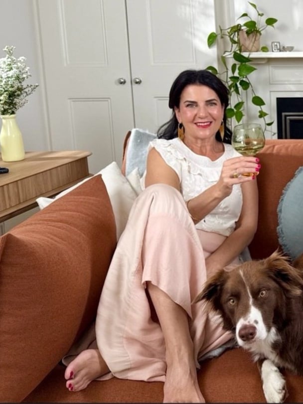 Marion sits on her couch with a glass of wine and her dog.