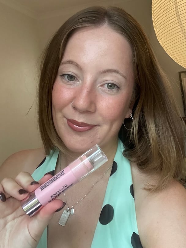 Selfie of Lucy with completed makeup holding up bronzer stick.