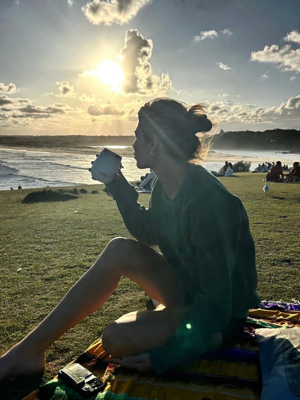 Megan sitting on a picnic blanket on grass near the beach.